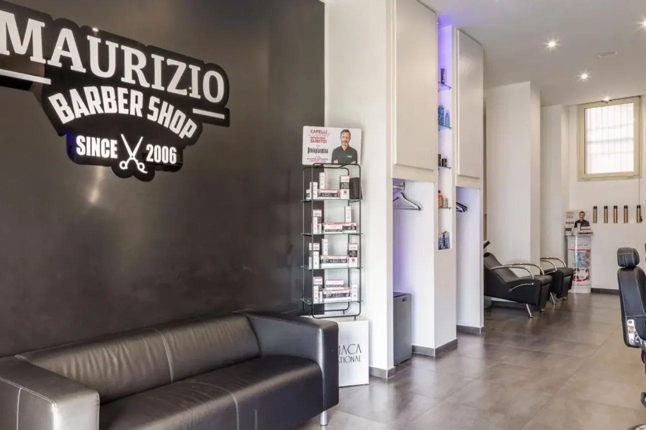 Zona attesa con divano e logo Maurizio Barber Shop